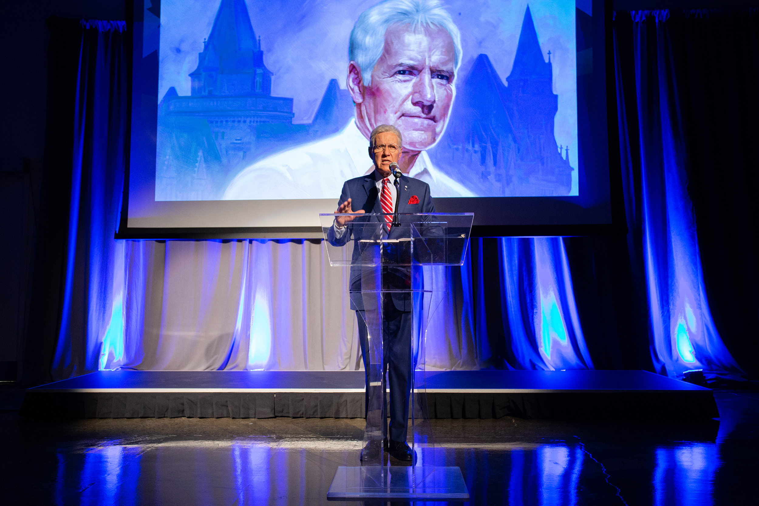 Alex Trebek stands at a podium on a stage