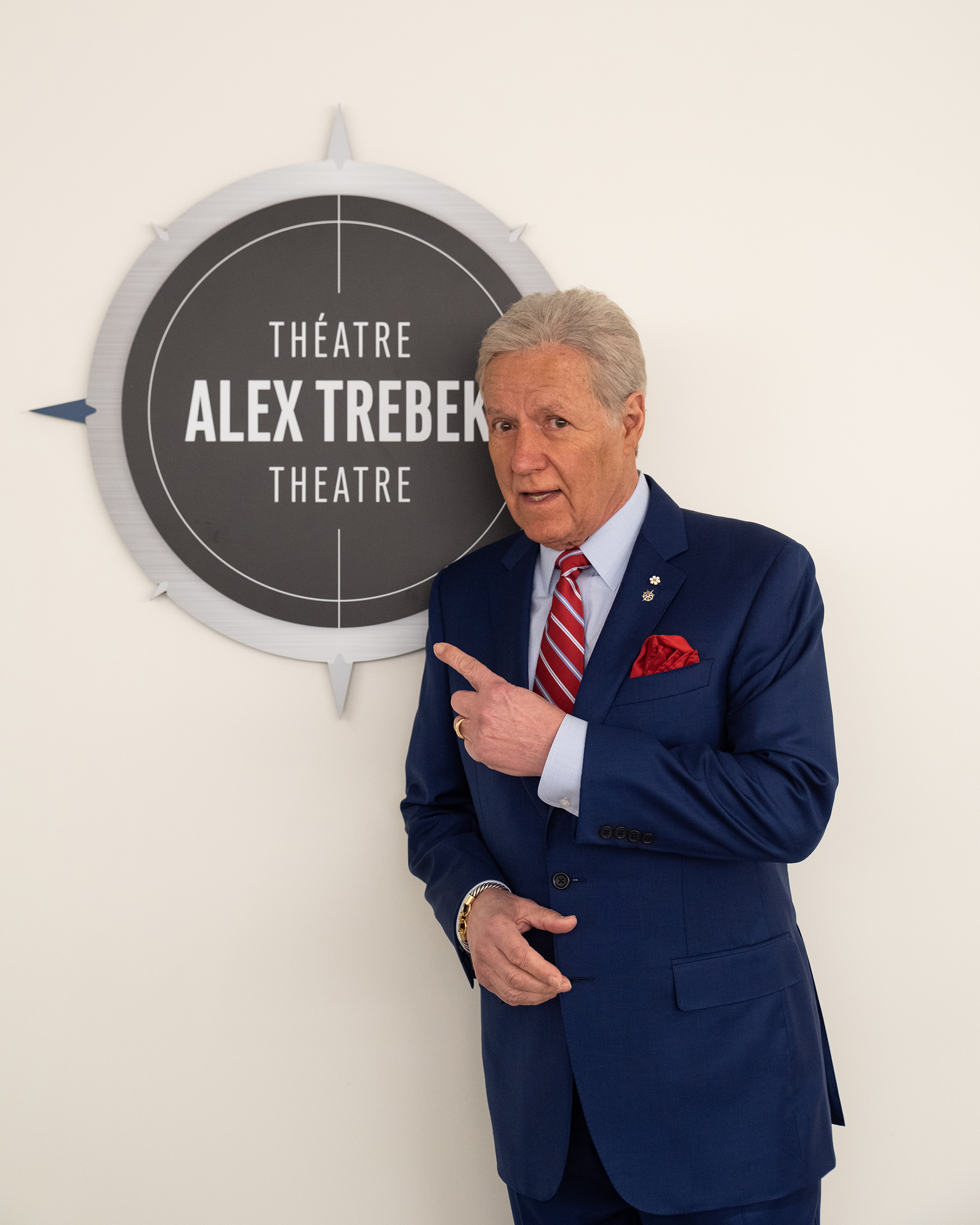 Alex Trebek stands next to a sign that reads "Théatre Alex Trebek Theatre"