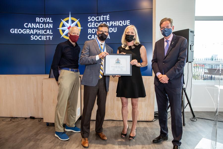 Photo: Ben Powless/Canadian Geographic Four people pose in front of a blue background saying "Royal Canadian geographical Society." They are Dr. Joe MacInnis, Gavin Fitch, Catherine McKenna, and John Geiger