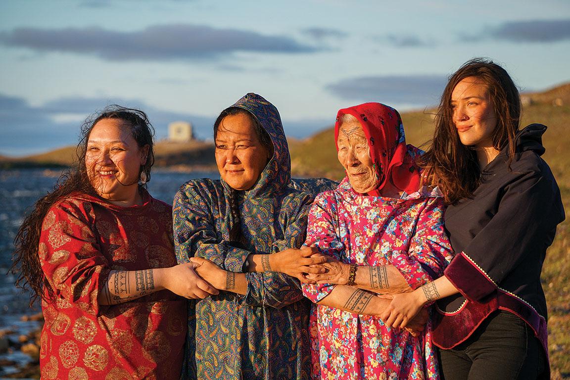 four inuit women stand on the shore showcasing their tattoos